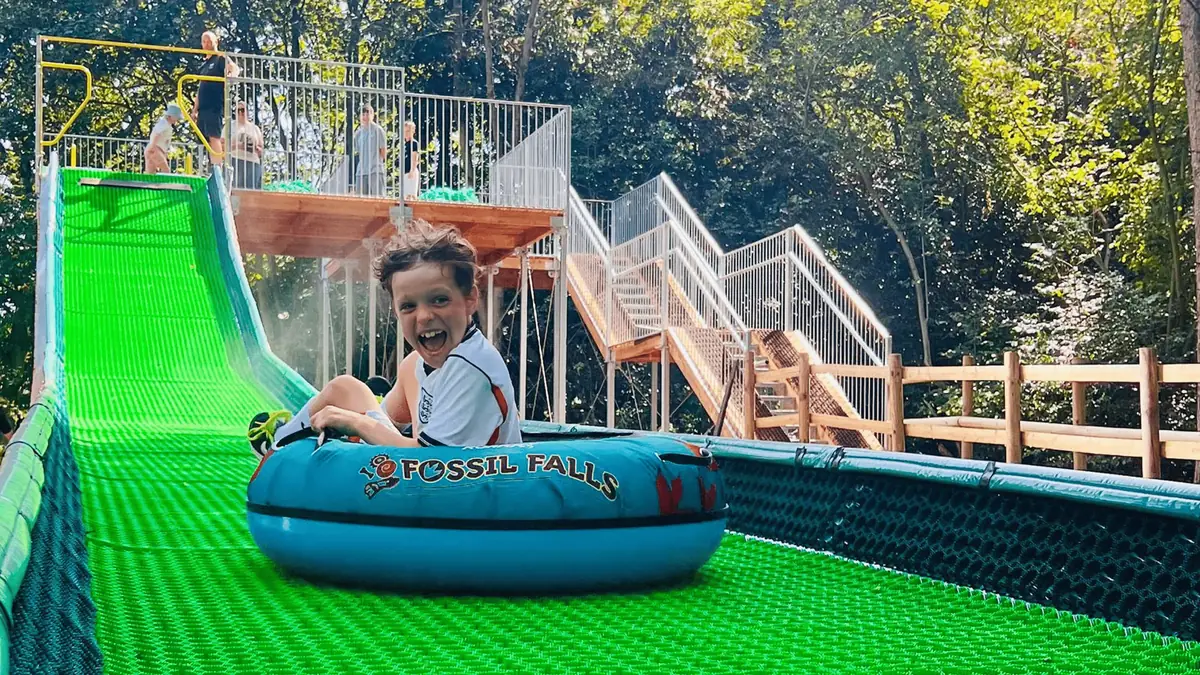 A boy laughing on a tube on a green tubing slide