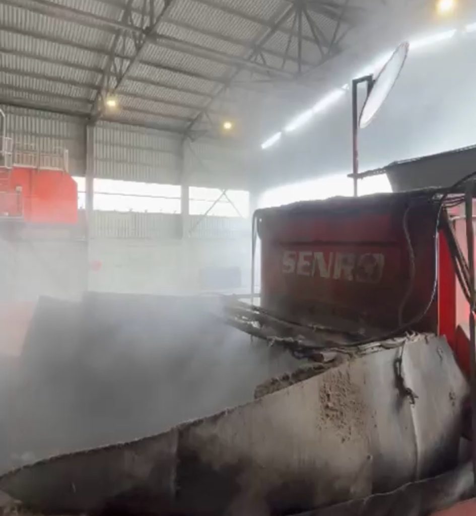 Water mist spreading over a conveyor and hopper inside an industrial hall, from a high pressure odor suppression line