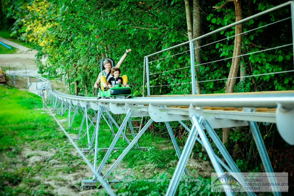 The raised Birštonas alpine coaster track running down the hill with a rider