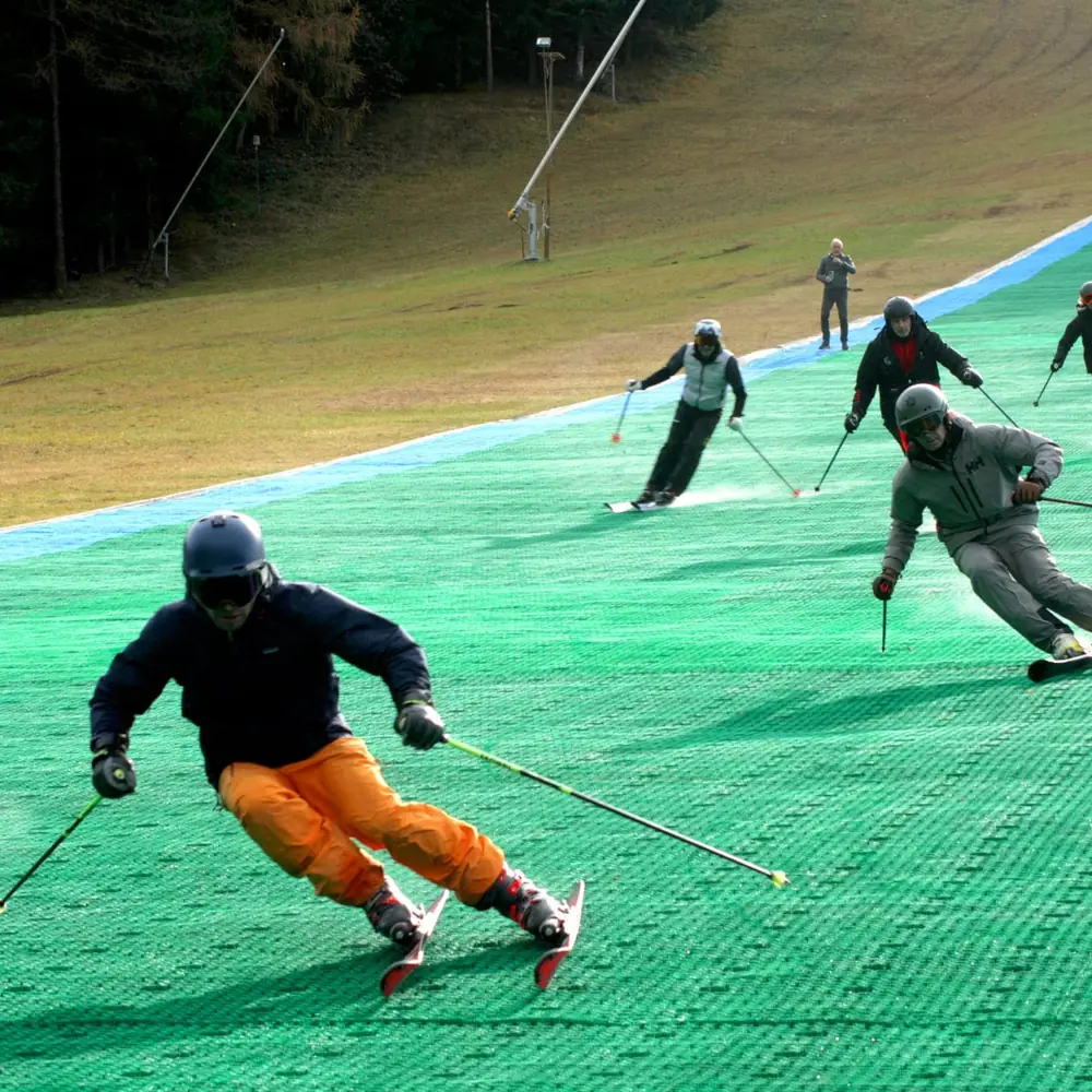 Skiers on a green Neveplast dry ski slope at Presolana Ski Arena, Italy
