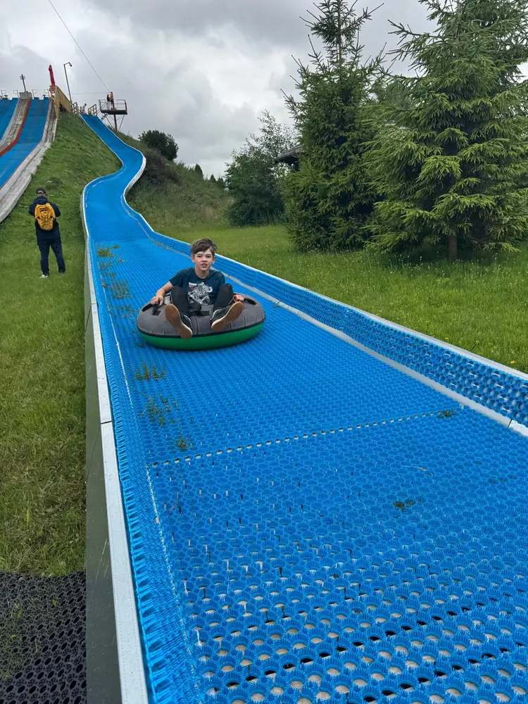 A boy in a tube riding down a blue tubing lane on a grassy hill