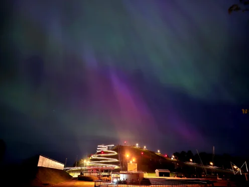 The lit Ventspils alpine coaster under the northern lights at night